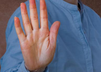 Person mit blauem Hemd hebt abwehrend die Hand