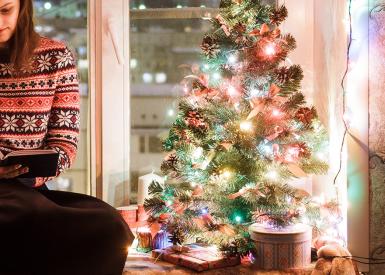 Frau liest Buch neben Weihnachtsbaum