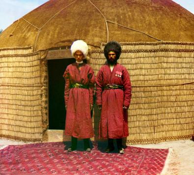 Zwei Männer stehen vor einer Jurte auf einem farbenprächtigen Teppich
