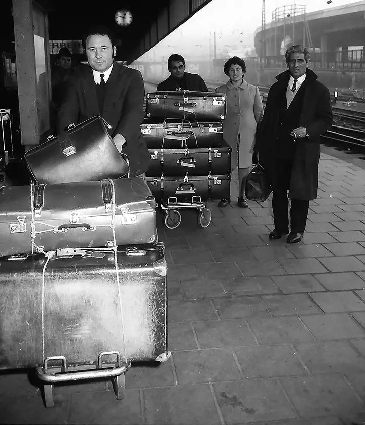 Menschen auf Gleis mit Koffern auf Gepäckwagen