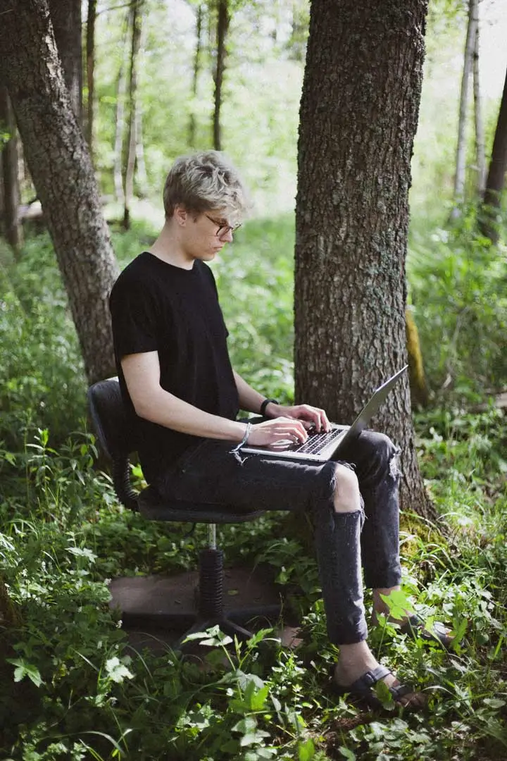 Person mit Laptop auf Bürostuhl im Wald