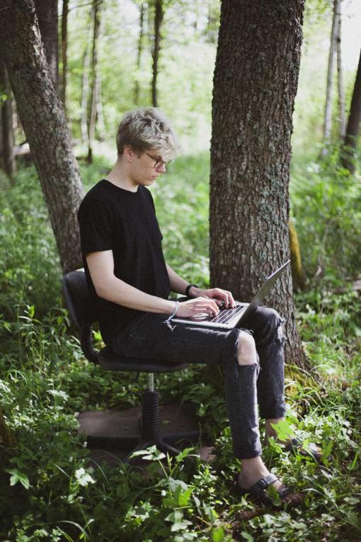 Person mit Laptop auf Bürostuhl im Wald