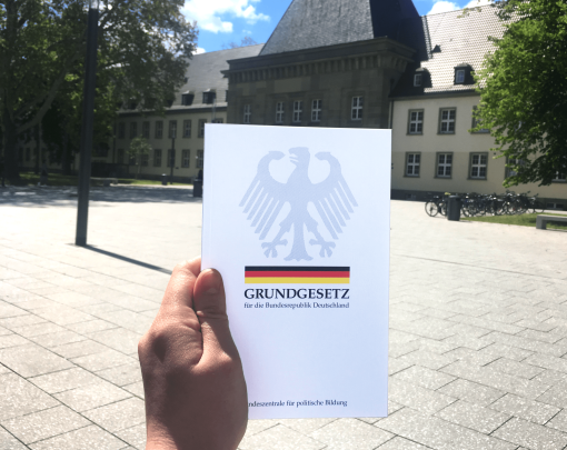 Image matching this topic Hand hält Grundgesetz mit Blick auf Uni-Forum