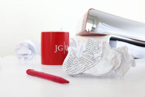 Image matching this topic JGU-Tasse, zerknülltes Papier, Stift, Ordner